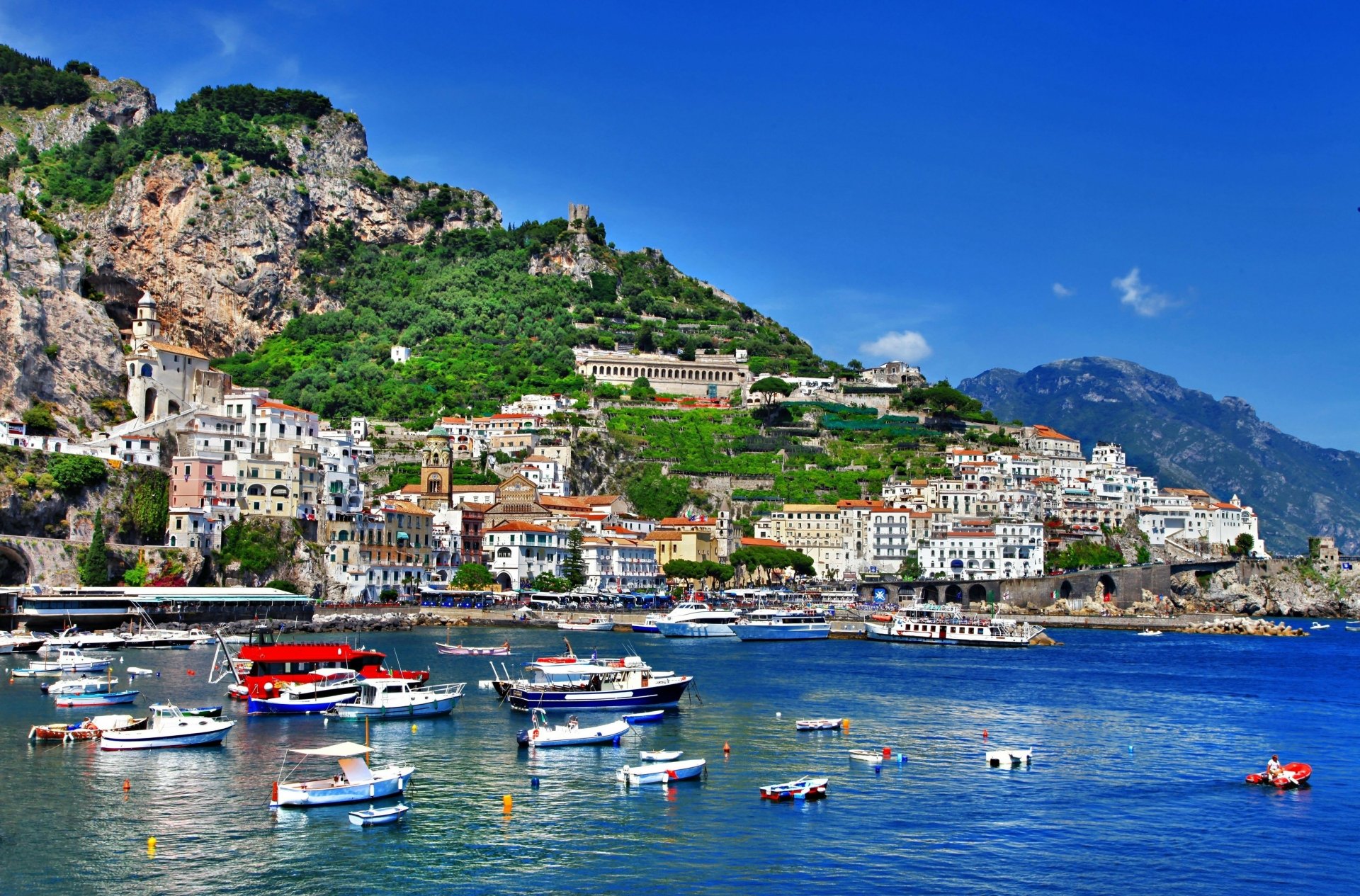 Casario, igreja e barcos em uma cidade litorânea europeia.